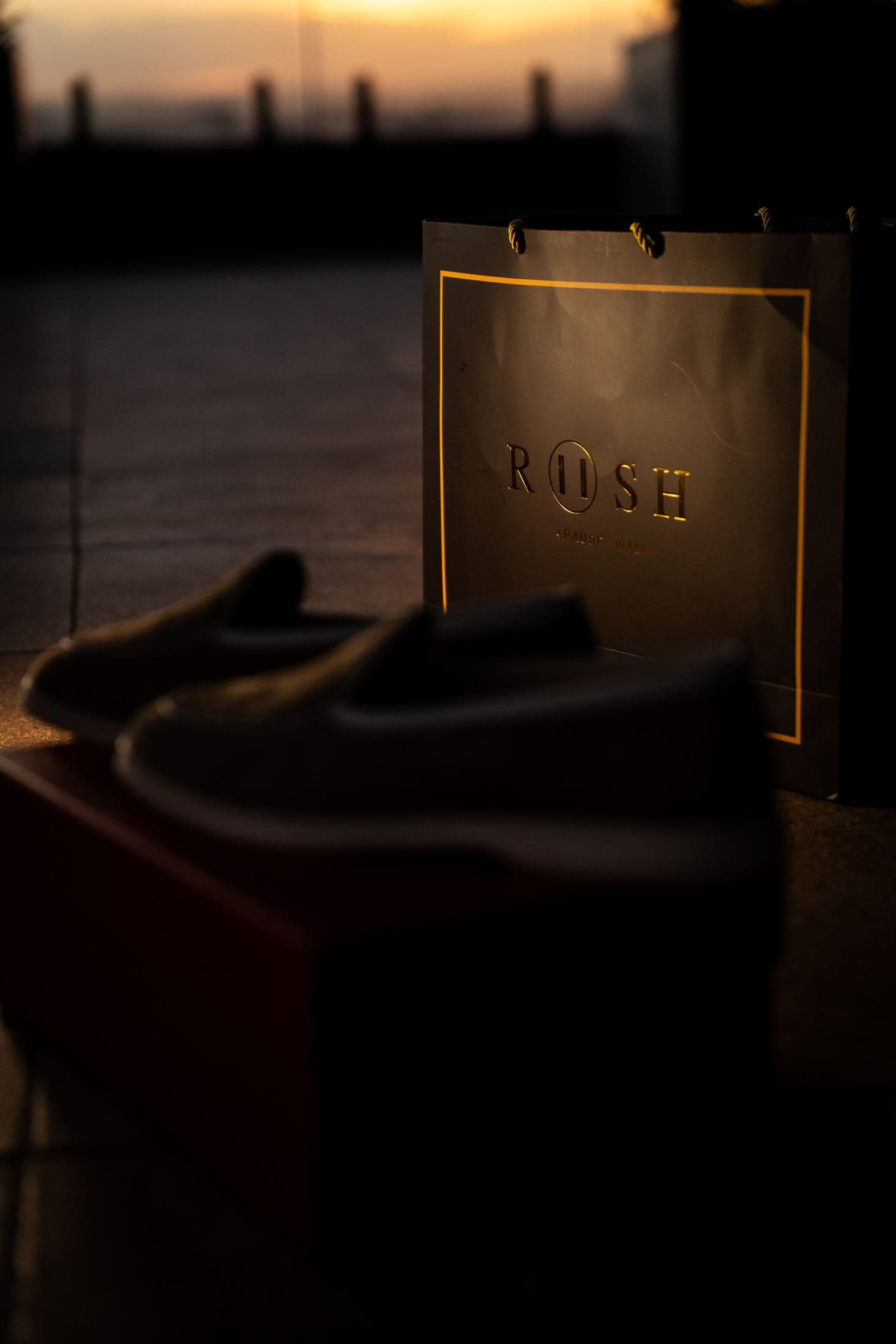 A RUSH bag lit from within at sunset, a pair of suede slip-ons beside it